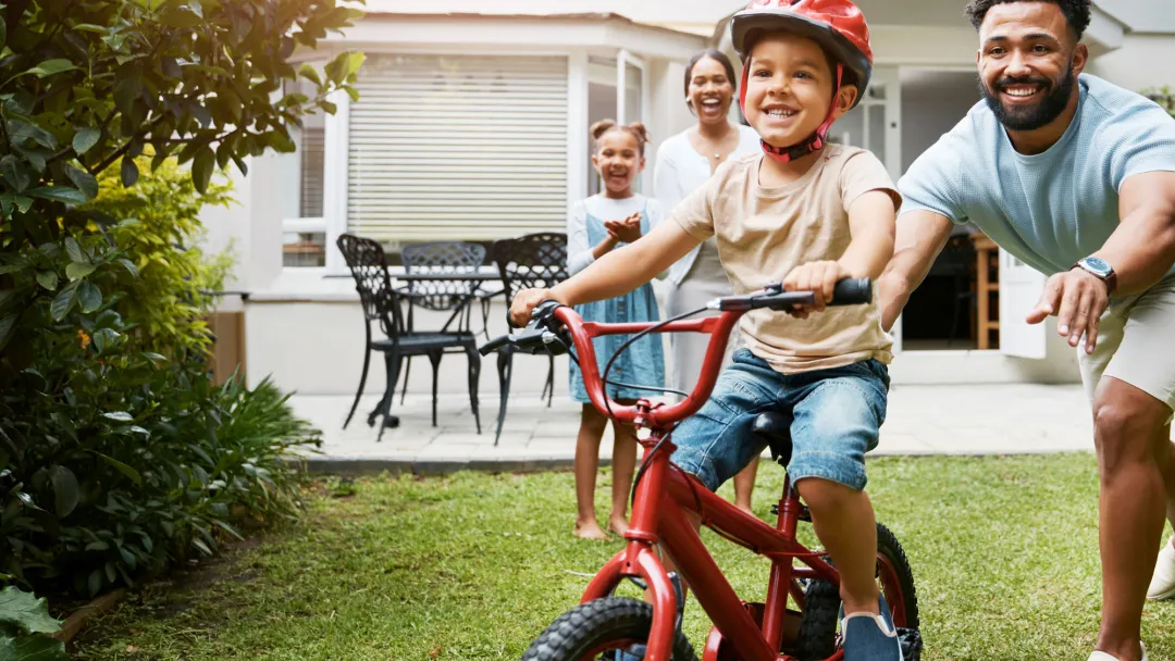 Family teaching son to ride bike in yard