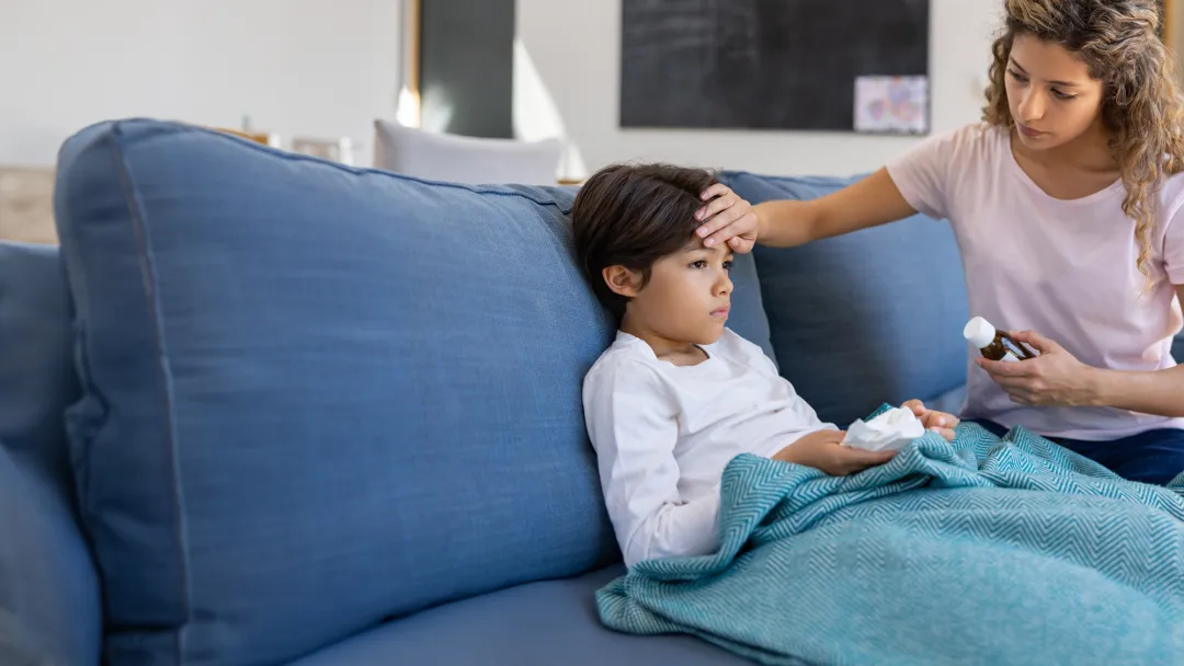 Mother at home checking if her sick son has fever by touching his forehead