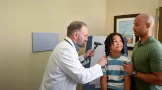 A Centra Care Provider Checks a Child Patient's Ears While His Father Supports Him