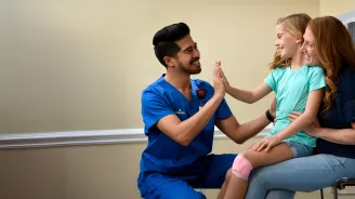 A Child Patient Sits in Her Mother's Lap While a Physician High Fives Her
