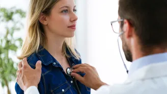 Doctor listening to woman's heart, a hand on her shoulder and a stethoscope 