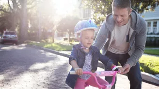 Father teaching his young daughter how to ride a pink bike in the street.