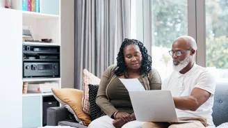 Man and woman reviewing paperwork with computer on lap