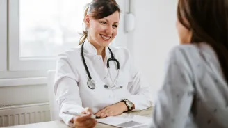 A friendly doctor meets a patient for the first time. They are both sitting at a desk, facing each other.