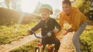A mom pushes her son a bike, outside.