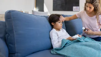 Mother at home checking if her sick son has fever by touching his forehead