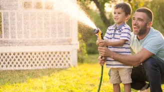 A Father and Son Spray a Garden Hose in the Front Yard as They Laugh
