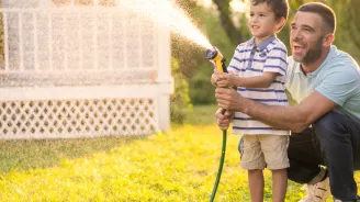 A Father and Son Spray a Garden Hose in the Front Yard as They Laugh