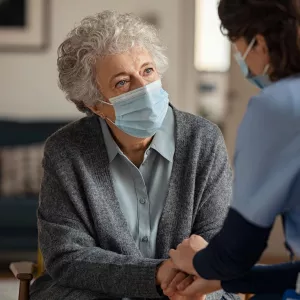 Hospice worker in mask, talking to elderly patient