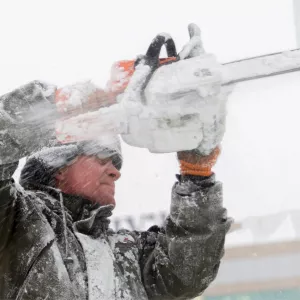 A man using a chainsaw to cut ice.