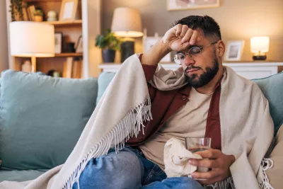 Man sitting at home on the couch wrapped in a blanket while sick with the flu.