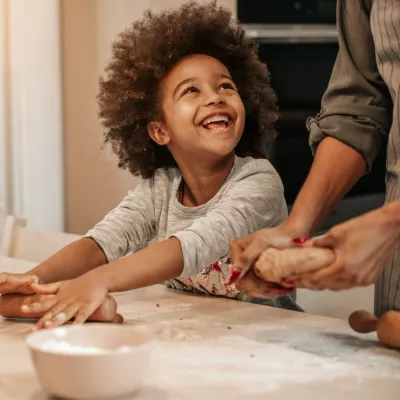 A Young Child Helps Their Parent Roll Out Dough to Make Muffins