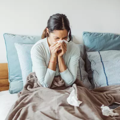 A Woman Blows Her Nose While Sitting Up in Bed