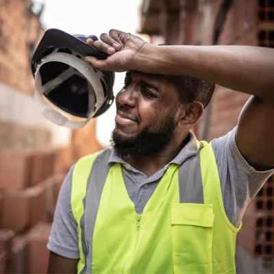 An Over Heated Construction Worker Removes His Hard Hat to Wipe His Brow