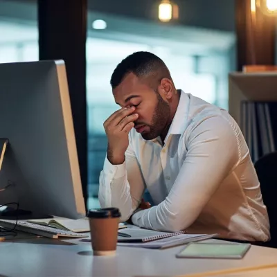 A Man Rubs the Bridge of His Nose with His Eyes Closed in Front of a Computer