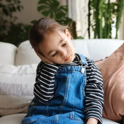 A Small Child Sits on a Couch at Home Holding Her Ear