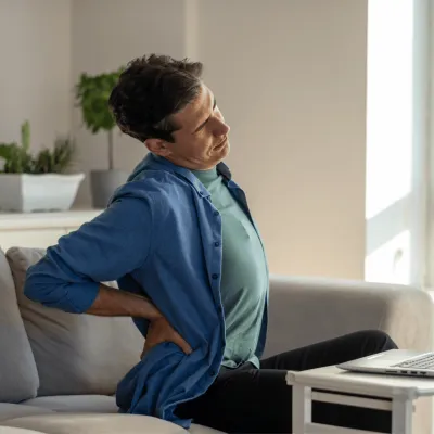 Man sitting on sofa in living room with back pain trying to ease tension