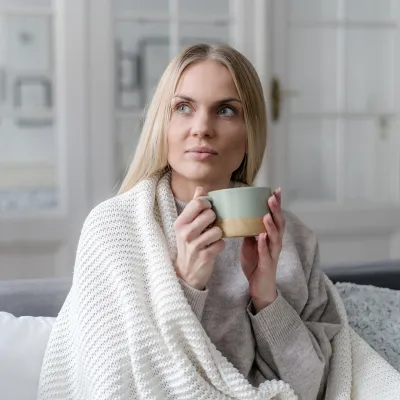 Woman holding cup of coffee while covered in a blanket