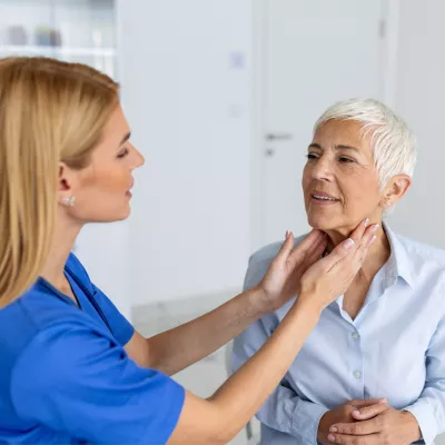 Doctor feeling the neck of a woman to check her thyroid.