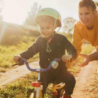 A mom pushes her son a bike, outside.