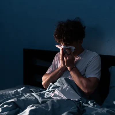 Sick man blowing his nose in bed