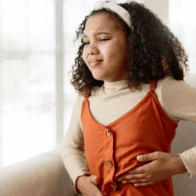 A young girl holding the left side of her abdomen in discomfort while sitting at home.