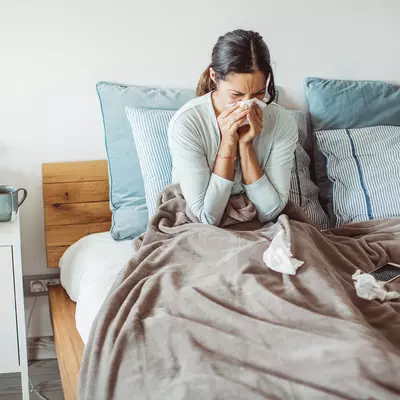 A woman sneezes as she sits sick in her bed