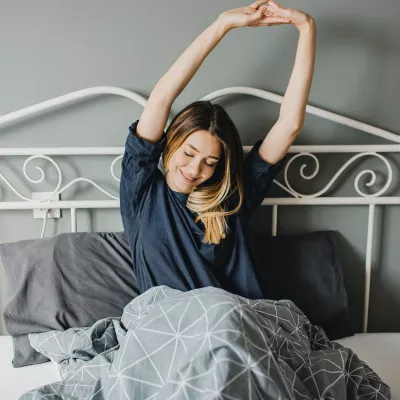 A woman stretching in bed after a good night's sleep.