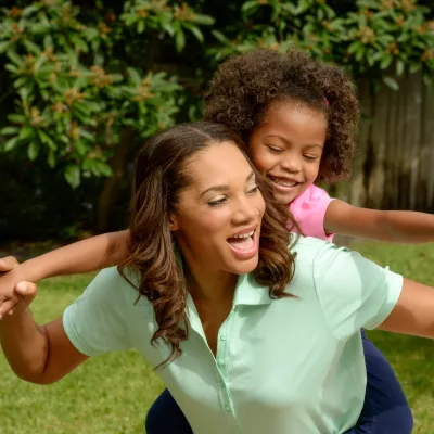 A mother carries her daughter on her back while playing outside. 