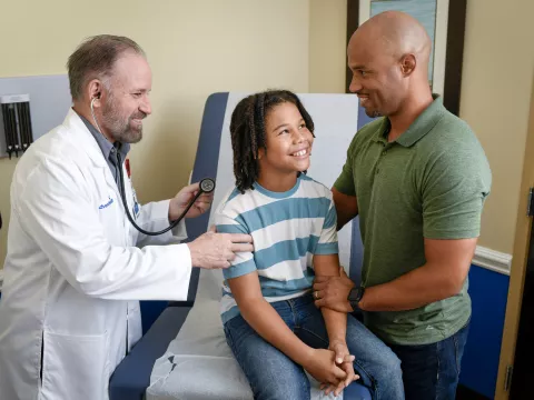 A Provider Checks a Child Patient's Breathing While His Father Supports Him