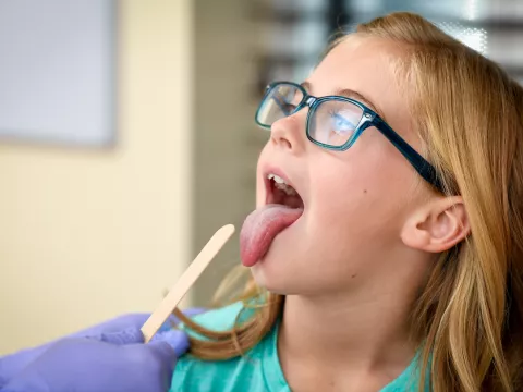 A Centra Care Patient Sticks Out Her Tongue as a Tongue Depressor Comes Into View