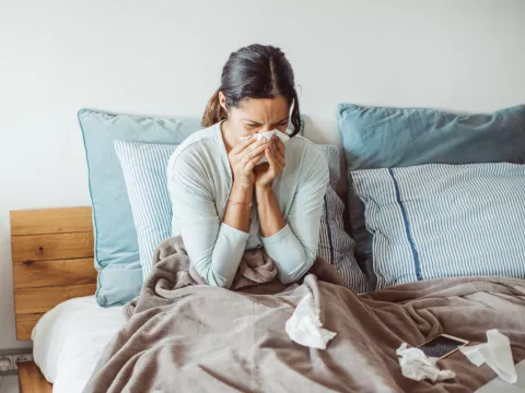 A Woman Blows Her Nose While Sitting Up in Bed