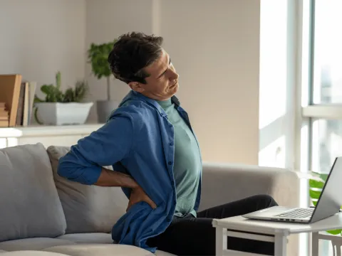 Man sitting on sofa in living room with back pain trying to ease tension