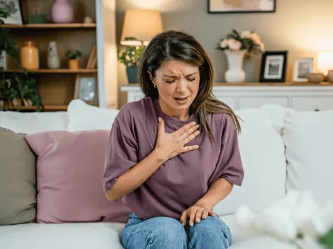 Woman Sitting on her couch clutching her chest with pain