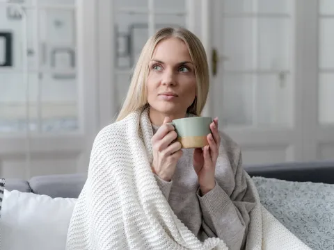 Woman holding cup of coffee while covered in a blanket