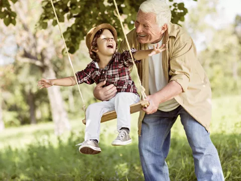 Grandfather pushes grandson on a tree swing