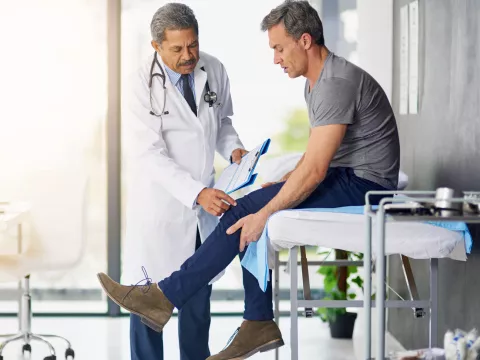 Doctor checking a male patient's knee.