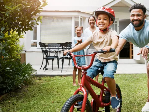 Family teaching son to ride bike in yard