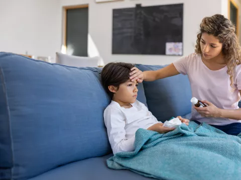 Mother at home checking if her sick son has fever by touching his forehead