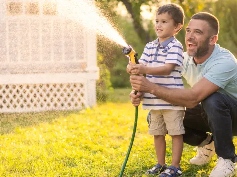 A Father and Son Spray a Garden Hose in the Front Yard as They Laugh