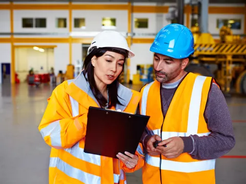 Two Warehouse Workers Talking Together Over a Clipboard.