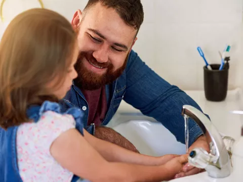 A dad teaches his young daughter how to wash her hands