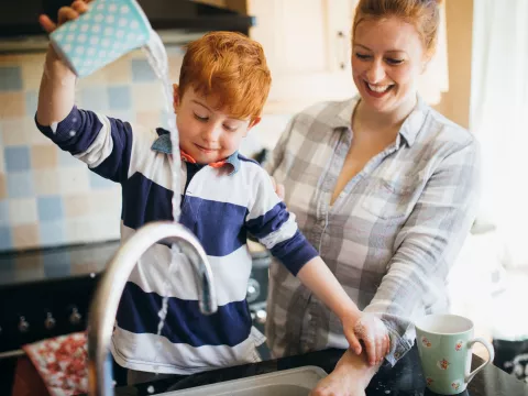 A mom and son wash dishes together.