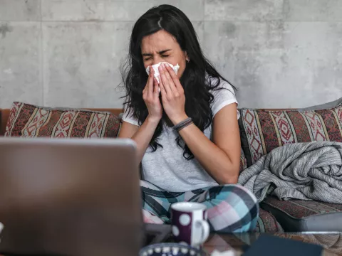 A woman sneezes into a tissue at home