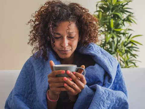 An adult black woman sips tea at home on her couch