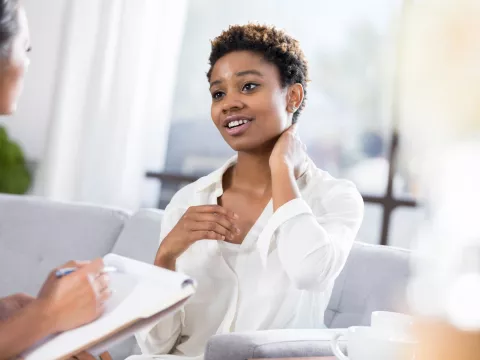 A young woman rubs her neck as she talks to a nurse