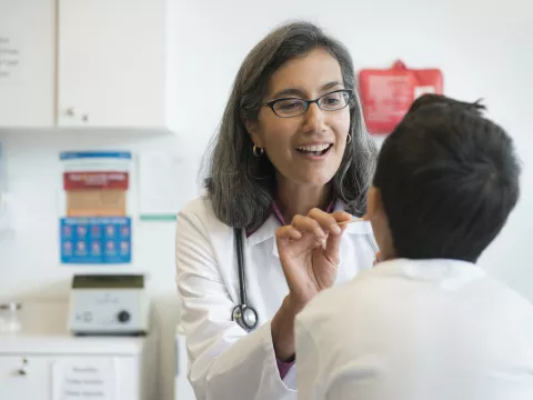 A female doctor looks into a young patient's mouth in an exam room.