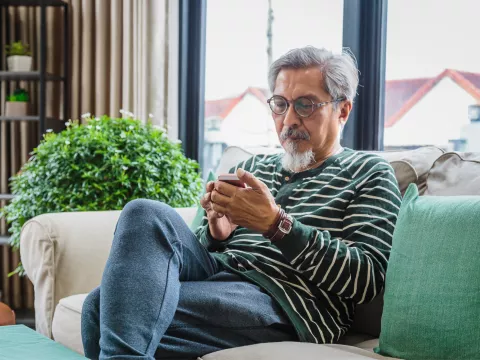 Older man sitting on a couch at home using a phone.