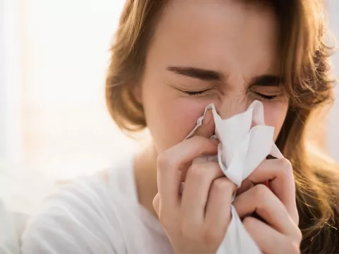A sick woman blowing her nose into a tissue.