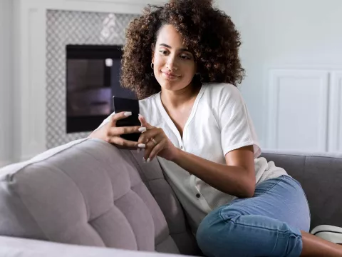 A woman on her cell phone at home on her couch.
